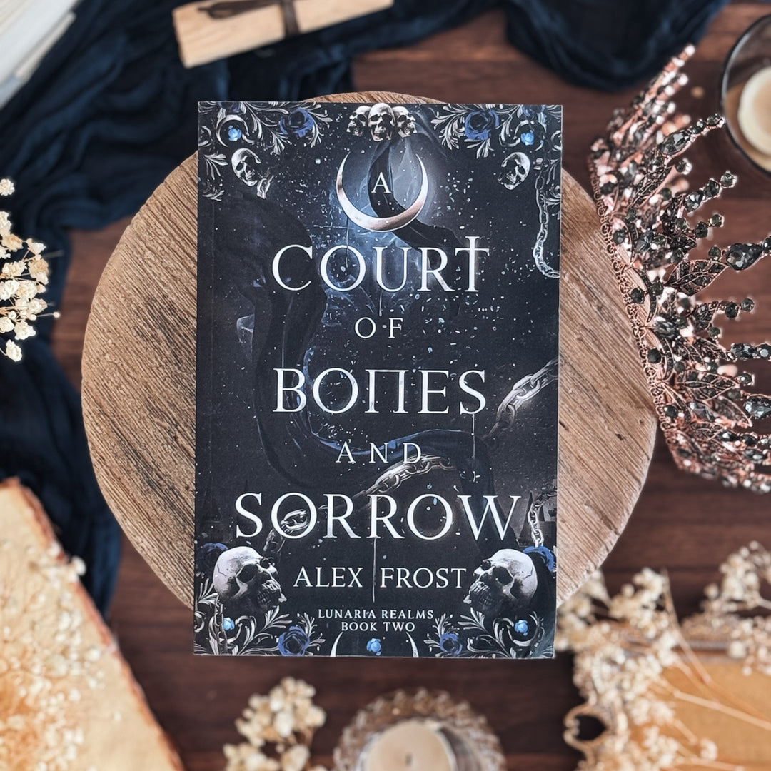 Book titled 'A Court of Bones and Sorrow' by Alex Frost on a decorative surface with skull and moon design.