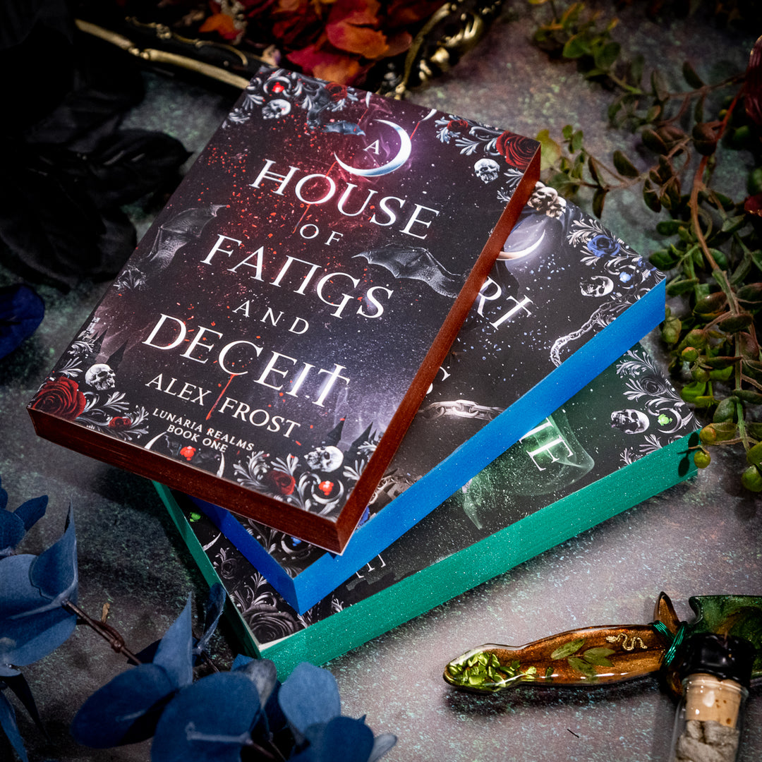 Stack of books titled 'House of Fangs and Deceit' by Alex Frost on a textured surface with decorative elements.