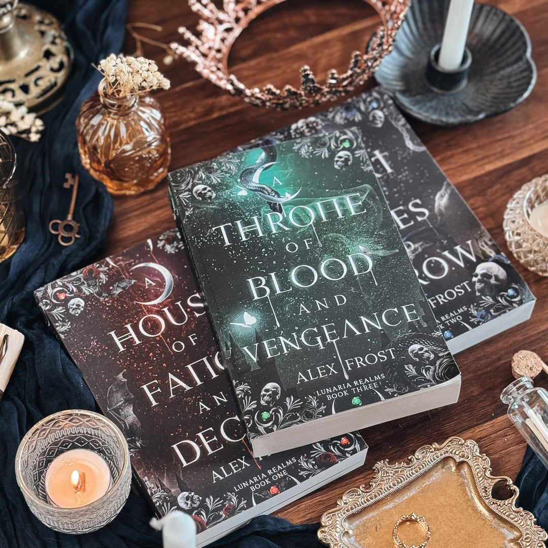 Two books titled 'A House of Fangs of and Deceit' and 'A Throne of Blood and Vengeance' on a wooden surface with decorative items.