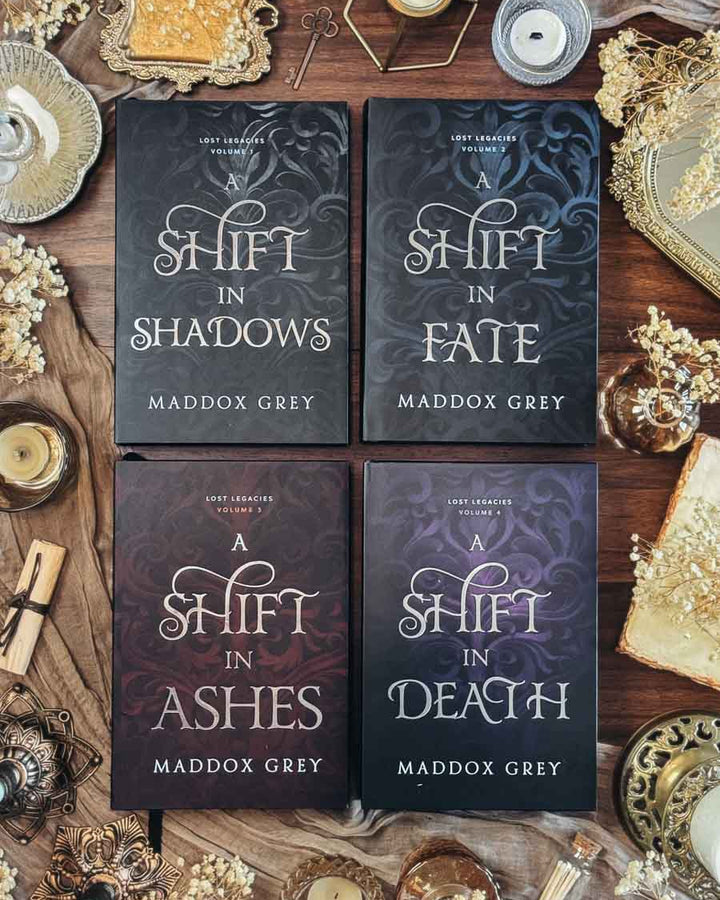 Four books titled 'Shift in Shadows', 'Shift in Fate', 'A Shift in Ashes', and 'A Shift in Death' by Maddox Grey on a wooden surface with decorative items.