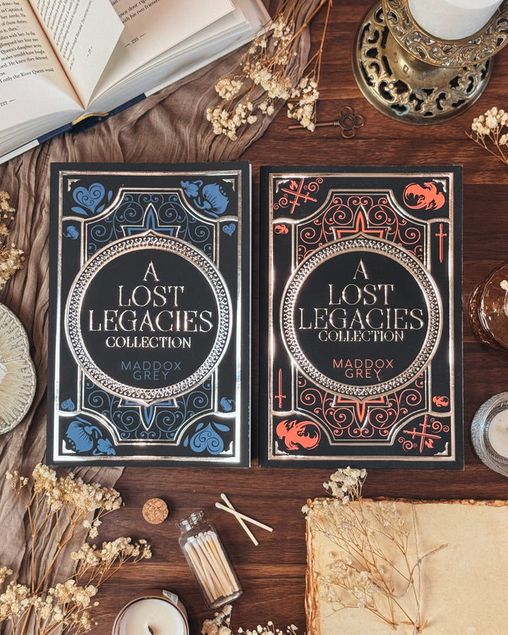 Two 'A Lost Legacies Collection' books by Maddox on a wooden surface with candles and dried flowers.