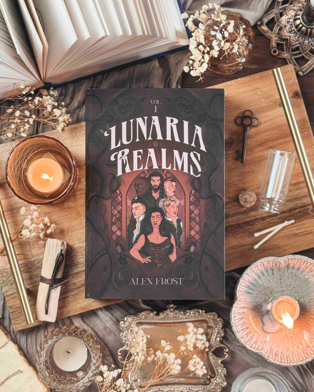 Book titled 'Lunaria Realms' by Alex Frost on a wooden surface with candles and flowers.