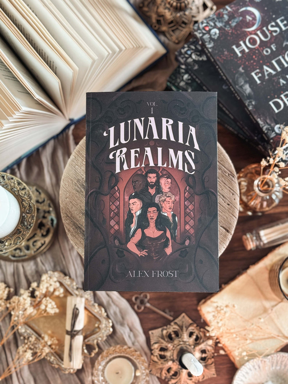 Book titled 'Lunaria Realms' by Alex Frost on a decorative surface with candles and books.
