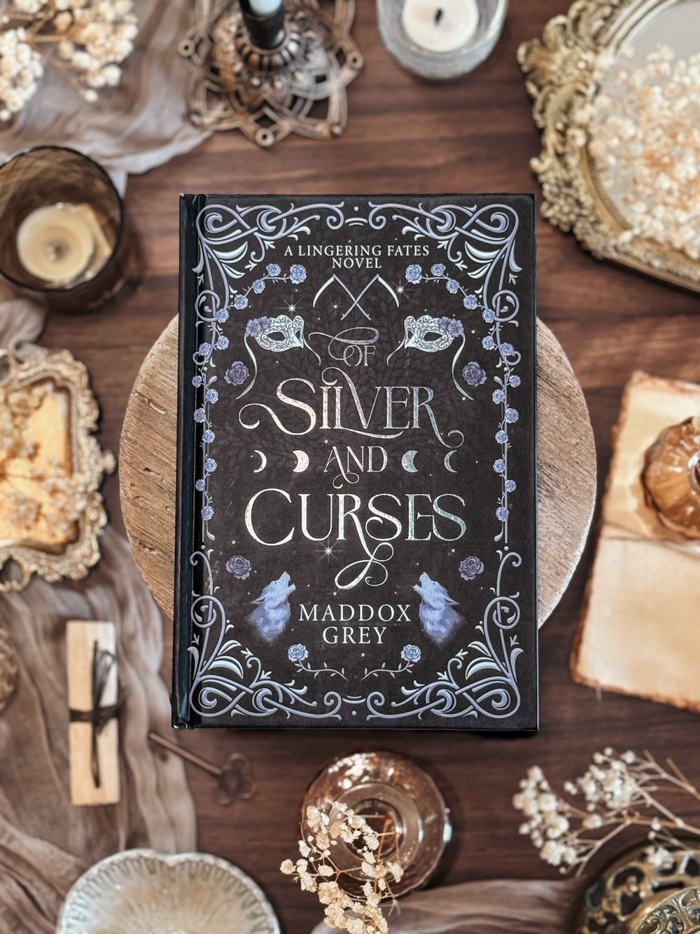 Book titled 'Silver and Curses' by Maddox Grey on a decorative surface with candles and ornaments.