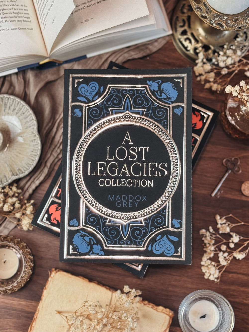 Book titled 'A Lost Legacies Collection' by Maddox Grey on a wooden surface with candles and books.